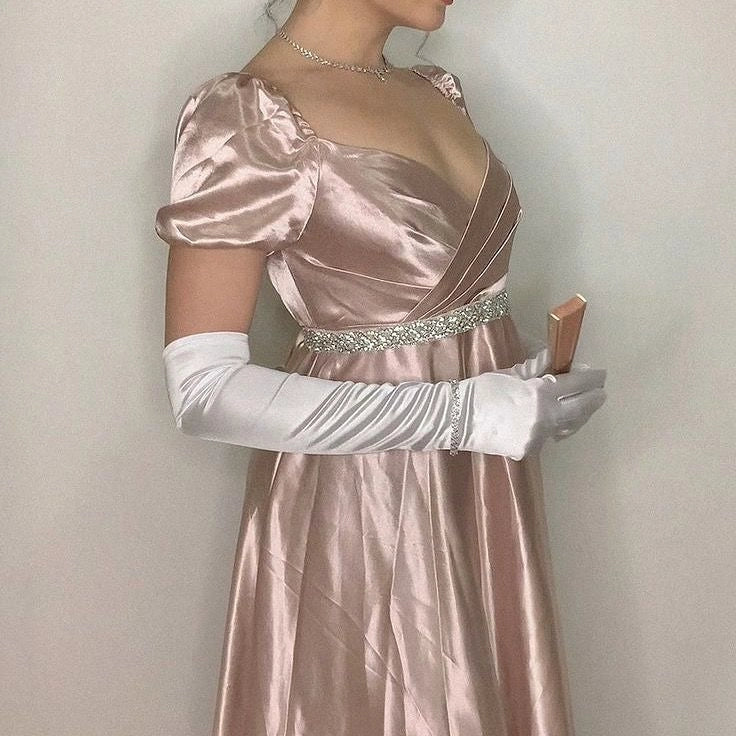 A light pink satin dress with a square neckline and bubble sleeves designed in a retro and elegant style, and a cross breasted rhinestone waistband outlining the curves,